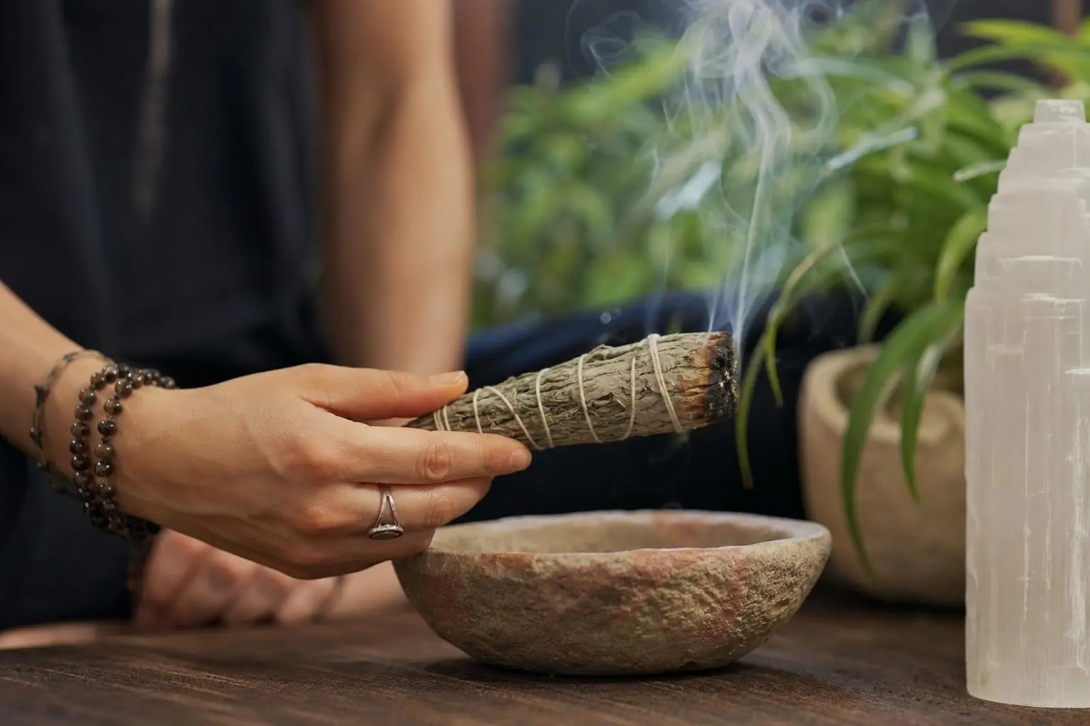 Personne tenant un bâton bouddhiste ou herbe de fumigation au-dessus d’un mortier, pratique de purification énergétique avec fumée légère.